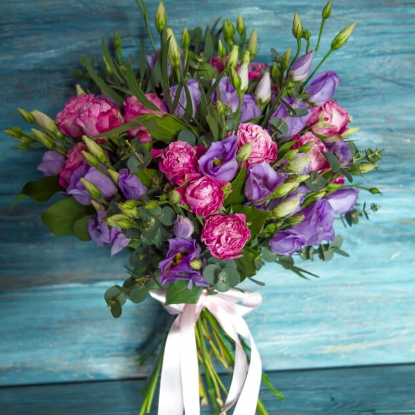 эустомы и розы в букете с белой лентой