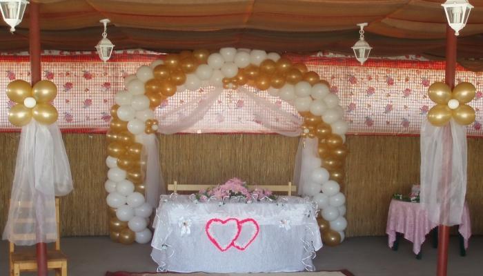 Широкая арка из белых и золотистых шариков, закрепленных над столом для молодоженов