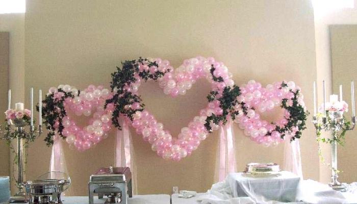Украшение в виде сердца из зеленых цветов и маленьких бело-розовых воздушных шариков